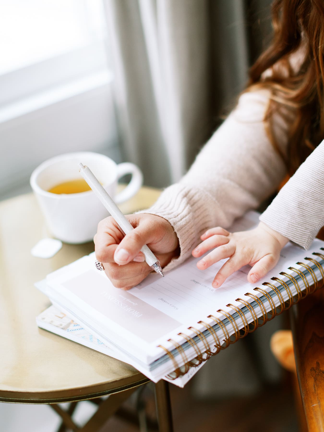 A working mom juggling her job and parenting, notebook, tea, and child sharing space.