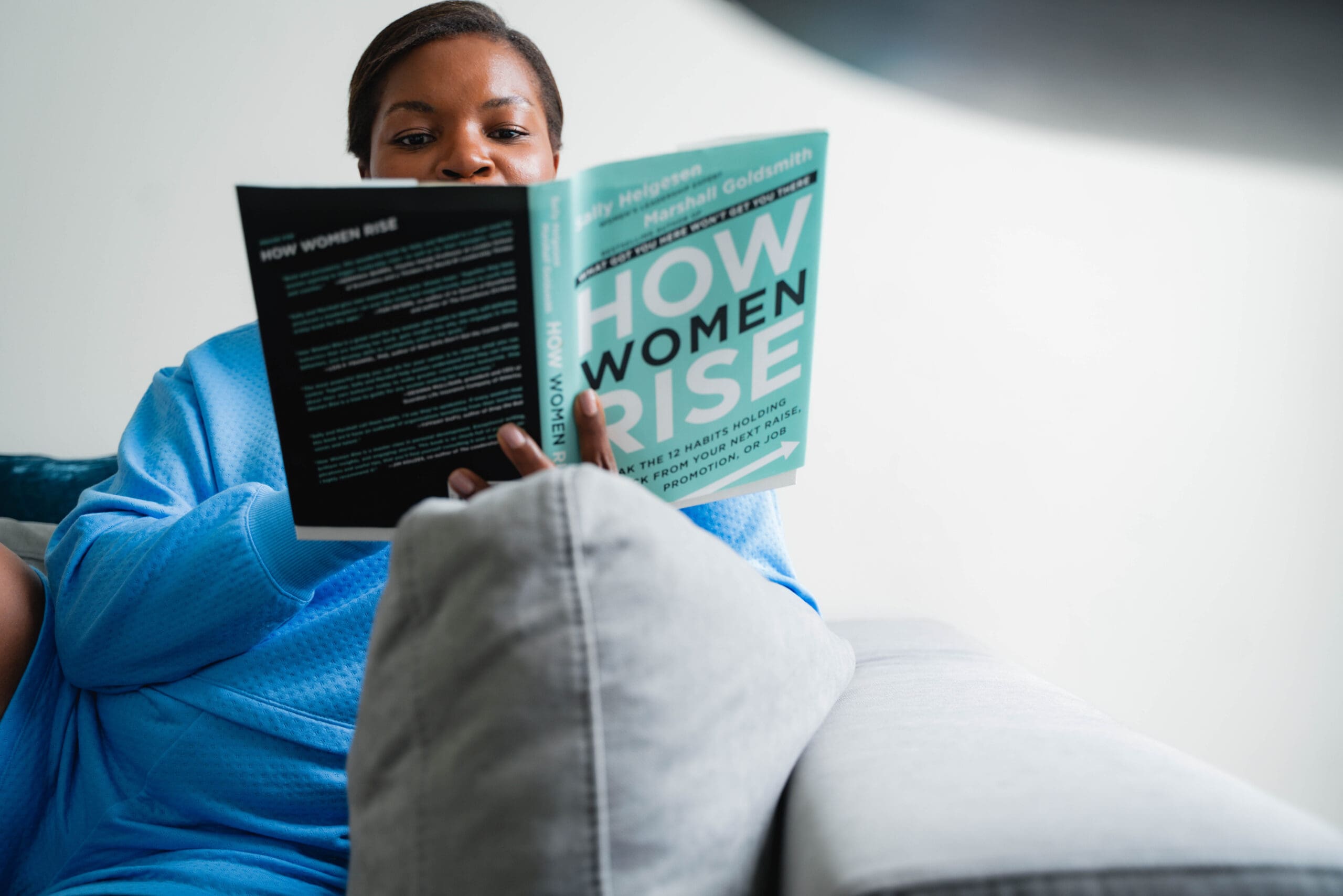 Career coach for professional women reading how women rise on gray couch